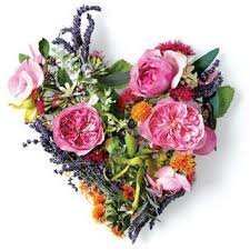 A heart-shaped arrangement made of assorted pink, orange, and purple flowers with lush green foliage on a white background—proof that Love Is In The Hair, celebrating radiant beauty like healthy skin and hair.