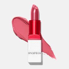 A pink Smashbox lipstick with its cap off, shown with a swatch of the same pink color behind it, on a plain light background—perfect for pairing with your favorite skin care routine.